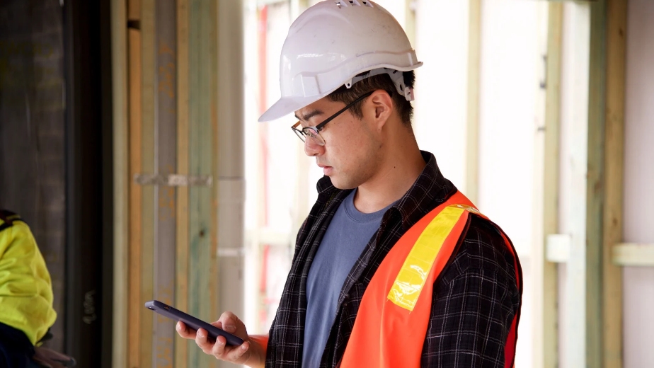 Step-by-Step Guide to Facebook, Construction worker wearing a hard hat and safety vest using a tablet on a job site.