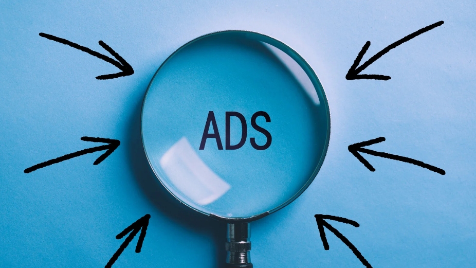 Magnifying glass over the word "ADS" with black arrows pointing toward it on a blue background.