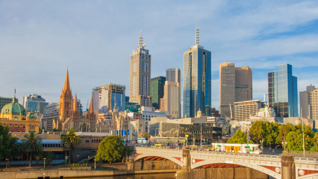 Top Suburbs to Target, Melbourne skyline featuring tall buildings, a river, and a bridge under a clear blue sky.
